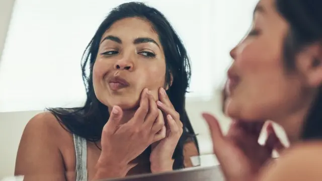 Девушка разглядывает кожу в зеркало