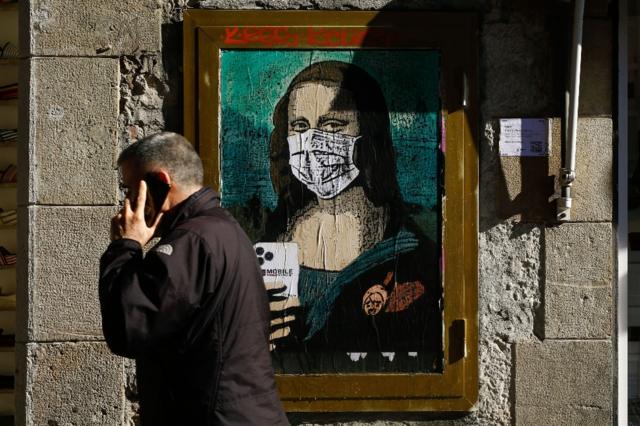 A man in Barcelona (Catalonia) walks past a poster depicting Leonardo da Vinci's Mona Lisa wearing a facemask, by Italian urban artist Salvatore Benintende