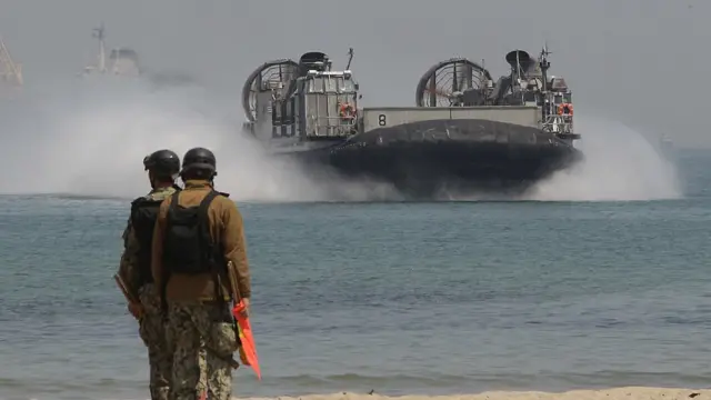 Un aerodeslizante llegando a la costa, donde lo esperan dos soldados