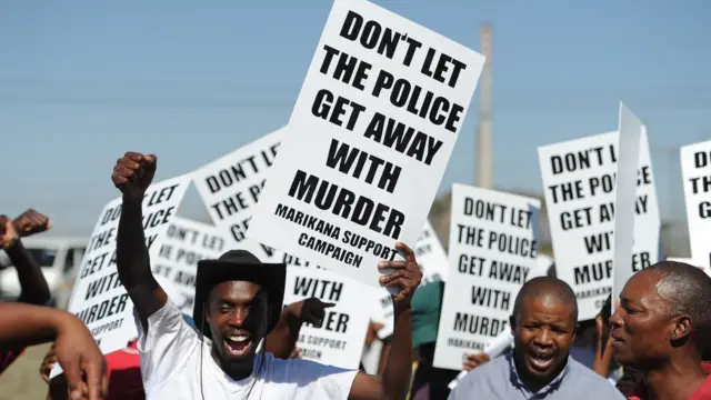 Waandamanaji wakionesha mabango yanayoshutumu polisi kusababisha mauaji ya wachimba migodi Marikana, Afrika Kusini, Oktoba 21, 2012