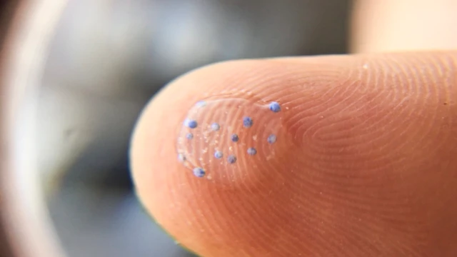 ภาพขยายแสดงให้เห็นชิ้นส่วนไมโครพลาสติกในหยดน้ำบนปลายนิ้วมือ
