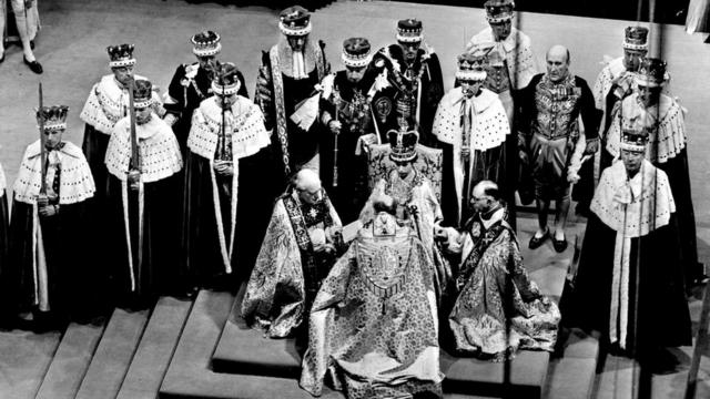 Fotografia colorida da coroação da rainha Elizabeth em junho de 1953 - ela está sentada no trono com a coroa real, cercada de homens com espadas e mantos cerimoniais