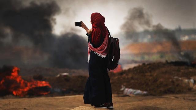 Mulher tira foto do local de confronto entre palestinos e israelenses em Gaza