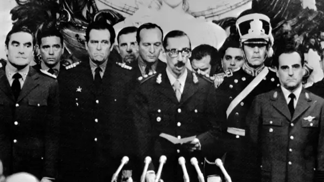 Varios militares están reunidos y uno de ellos se dirige al público