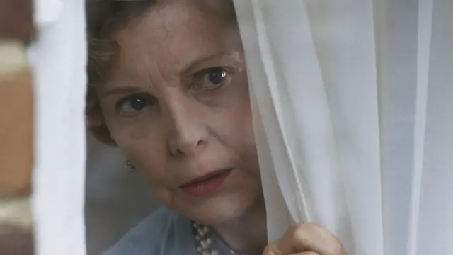 Žena gleda kroz prozor, drži zavesu