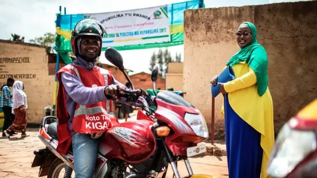 Women wear wear cloth of Rwanda flag colours dey smile as man sidon on top motorcycle