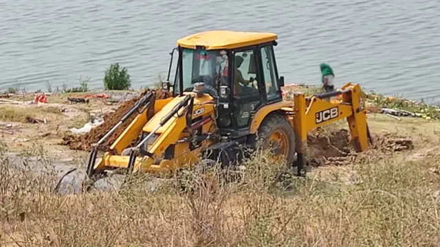 A digger creates a large pit by the banks of the Ganges