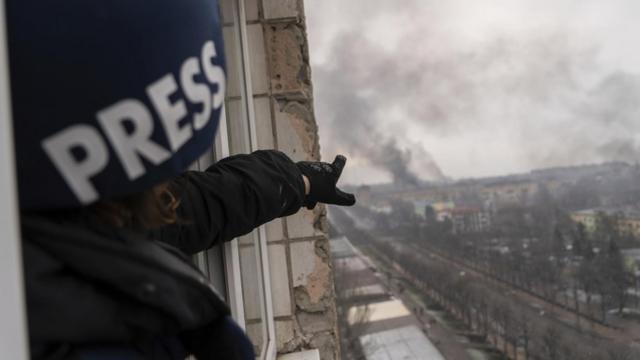 Евгений Малолетка указывает на дым, поднимающийся после авиаудара по родильному дому в Мариуполе