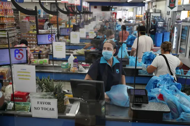 Una empleada en un supermercado en Miami, detrás de láminas de plexiglass