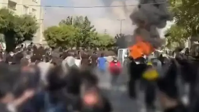 لقطة من مقطع فيديو نشره ناشطون معارضون يظهر محتجين على مقربة من مركبة مشتعلة في منطقة كرج غربي العاصمة الإيرانية طهران