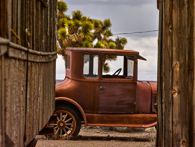 An abandoned car seen between two wooden buildings