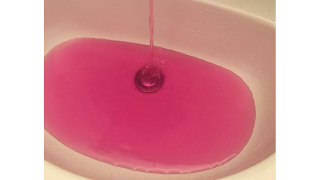 Detalhe da água completamente rosa caindo numa pia.