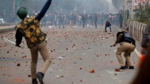 A riot police officer throws a piece of brick towards demonstrators during a protest against a new citizenship law in Seelampur, Delhi