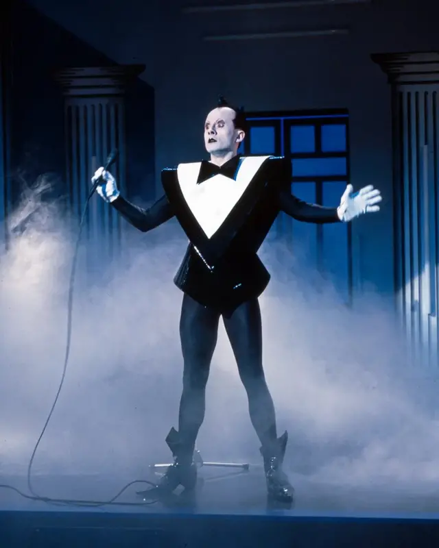 Nomi je bio poznat po svojim nastupima pod velikim naslagama šminke i obučen u plastični, crno-beli frak