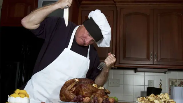 Мужчина с ножом и вилкой, пытающийся проткнуть сгоревшую индейку
