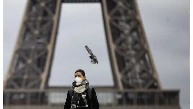 Una mujer con tapabocas frente a la Torre Eiffel,