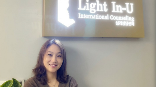 Julia stands next to a sign for her counselling centre, Light In-U.