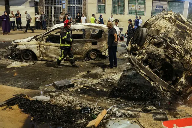 Des gens regardent des véhicules incendiés lors d'une manifestation menée par des jeunes réclamant des réformes dans les secteurs de la santé et de l'éducation à Salé, le 1er octobre 2025.