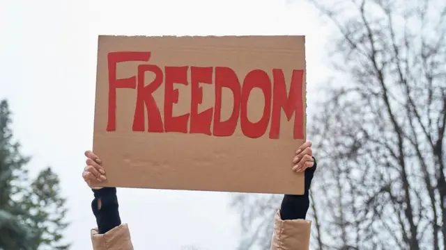 Tangan orang tak dikenal berdiri dengan spanduk bertuliskan 'Freedom'.