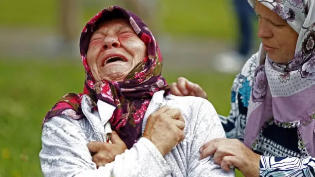 Familiar de víctimas de Srebrenica llorando amargamente mientras otra mujer intenta consolarla.