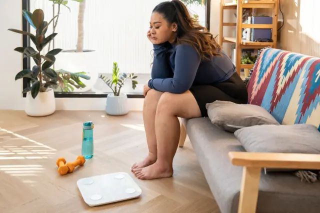 önünde tartı ile bir koltuğa oturmuş, eli çenesinde düşünceli bir kadın