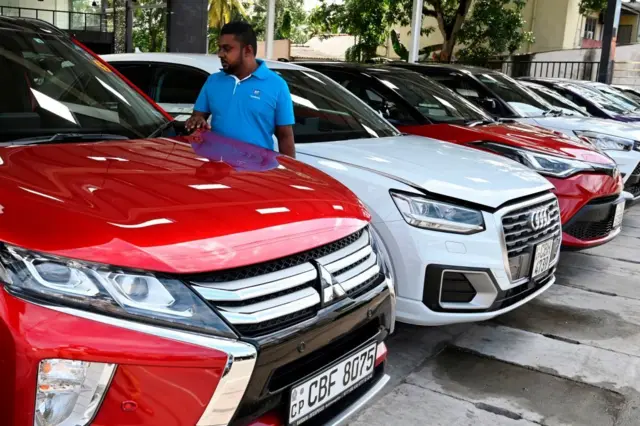 ලියාපදිංචි කළ වාහන අලෙවි කිරීමට තබා ඇති ස්ථානයක නිල් පැහැති ටීෂර්ට් එකක් ඇදගෙන සිටින පුද්ගලයෙකු
