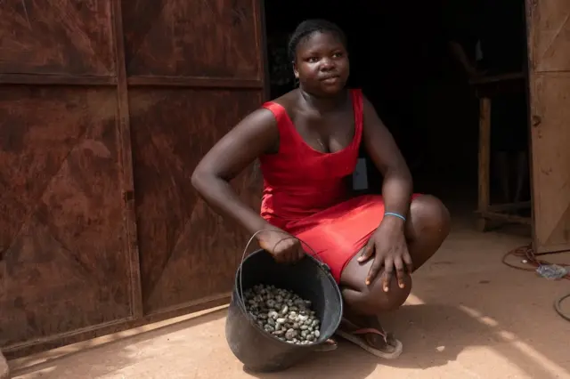 Alciony Fernandez, 14 ans, pose avec ses quatre kilos de noix de cajou de la ferme familiale qu'elle dit vendre à 350 CFA le kilo dans un petit magasin situé à l'extérieur de la capitale, Bissau, dispose d'une balance que les producteurs locaux de noix de cajou peuvent utiliser pour peser leur récolte. Elle a marché environ trente minutes jusqu'au magasin pour peser les noix de cajou.