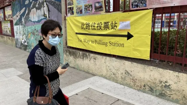 A woman walks past a sign pointing towards a polling station as Hong Kong votes for its legislative council, 19 December 2021
