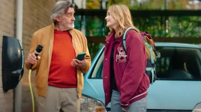 Mężczyzna z kablem do ładowania elektrycznego stoi przed samochodem elektrycznym z młodą kobietą