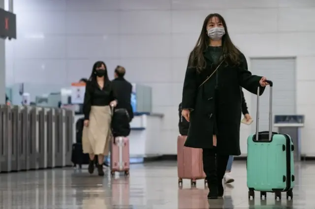 Mujeres asiáticas con barbijo en una terminal de transporte.