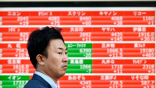 Asiático frente a una pantalla con la bolsa de valores