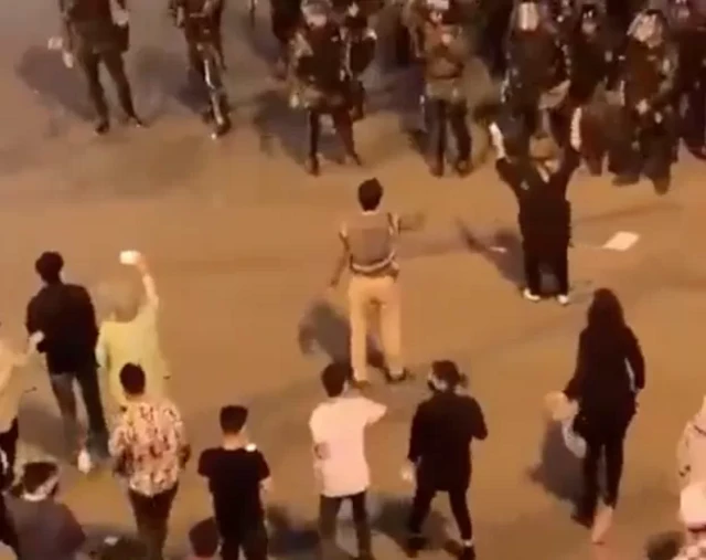 في هذه الصورة ، تظهر امرأة على اليمين ترفع يديها وتقول شيئًا لقوات الأمن الذين يتوجهون نحوها ، ولكن مرة أخرى يحيط بها الناس وينقذونها.