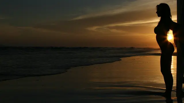 Silhuetatvbet saqueuma mulher na praia durante o entardecer