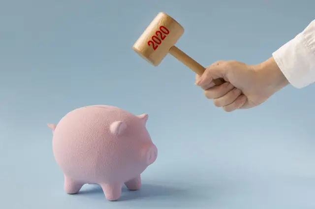 Un martillo que dice 2020 rompiendo un chanchito con ahorros