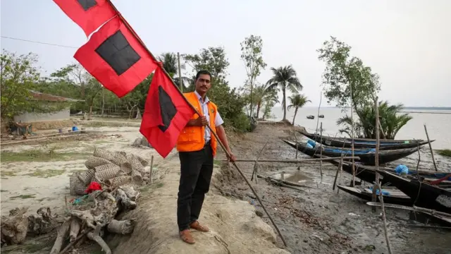 Sabastin Bachar, chef d'équipe du CPP pour le village de Chila, montre le système de drapeau à trois niveaux qui est affiché sur la place du village.