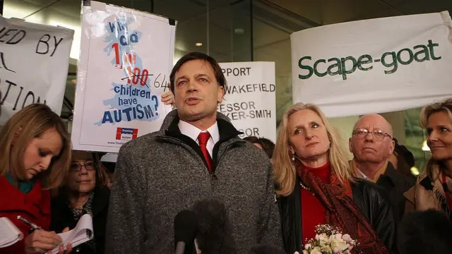 Andrew Wakefield parado com manifestantes ao ladojogo da motinha bet365uma placa dizendo "Cabra-bode" (sic)