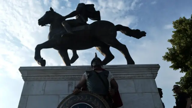 демонстрант в образе древнегреческого воина у статуи Александру в Пелле