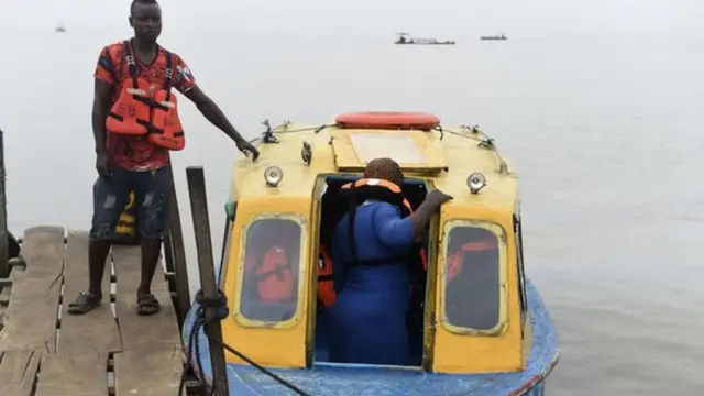 Fery operator stand dey wedge di ferry as passenger dey enta inside.