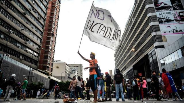 Joven venezolano con una bandera que dice: "No + dictadura".