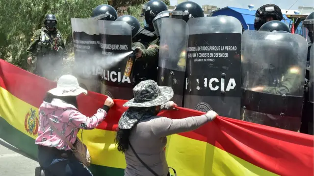 Un policía echa un gas en el rostro de una manifestante arrodillada.