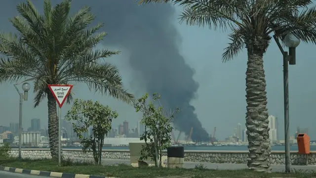 Palmiye ağaçları arasından gözüken bir limandan dumanlar yükseliyor. 