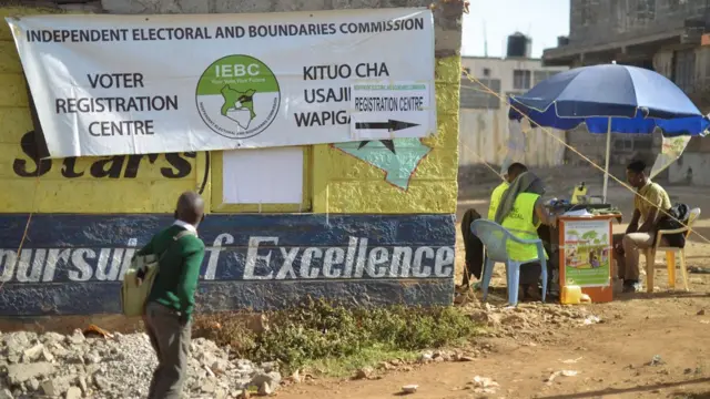 A school boy looks at a banner advertising a voter-registration point January 18, 2017 as he walks past as Interim Electoral and Boundaries Commission (IEBC) clerks capture the biometric details of a voter at Baba-Dogo slum area of Nairobi.