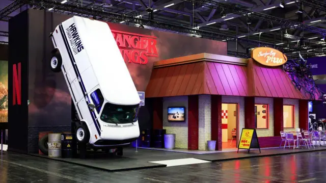 Stand de Stranger Things de Netflix en la Gamescom 2023 con una furgoneta blanca con el nombre de Hawkins.