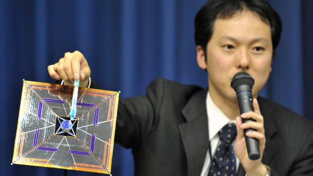 O cientista Yuichi Tsuda segurando um modelo do satélite IKAROS em uma conferência