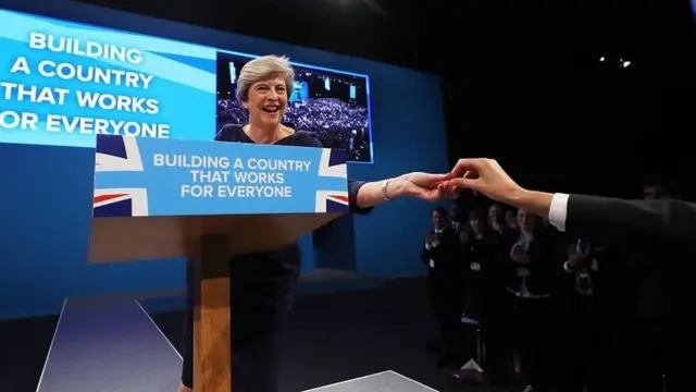 ハモンド財務相からのどあめを手渡されるメイ首相