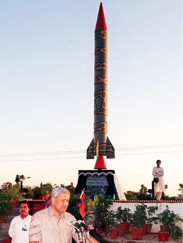 Khan hablando con un modelo de misil detrás suyo.