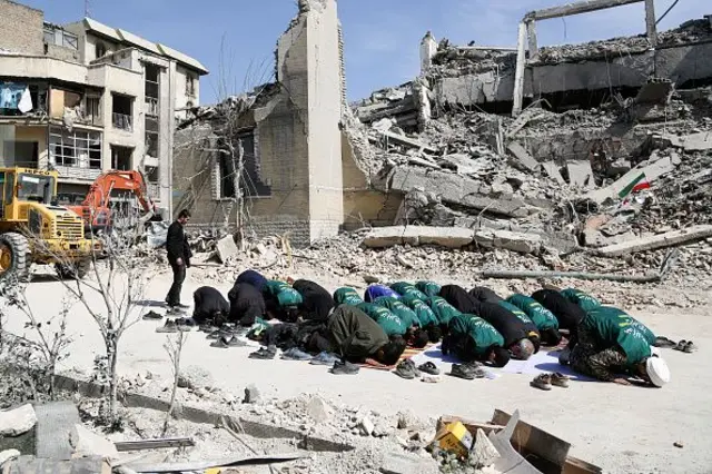 Іранські рятувальники моляться на тлі зруйнованого будинку