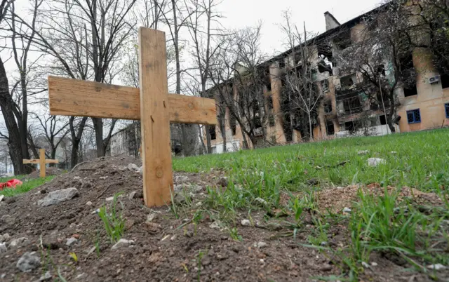 Dua makam di luar gedung apartemen yang hitam legam di Mariupol, Ukraina.