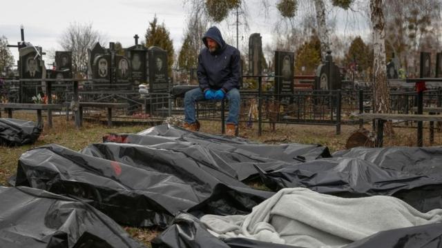Um funcionário do serviço funerário senta-se ao lado de corpos de civis em Bucha
