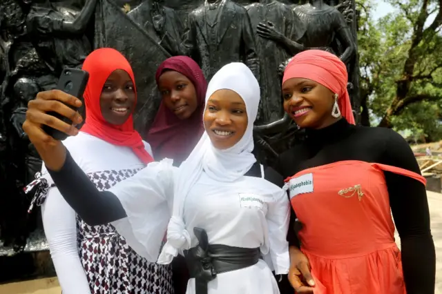 Muslim women wearing hijabs smile and pose for selfies.